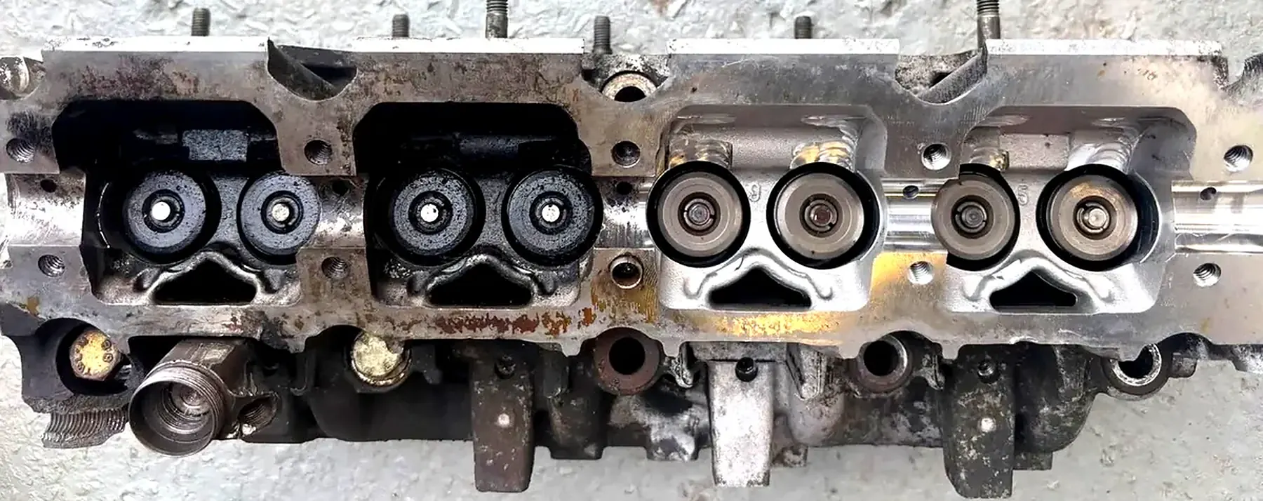 An engine part half cleaned with dry ice. The left half is still covered in black oil and burnt-on dirt. The right half is clean bare metal.